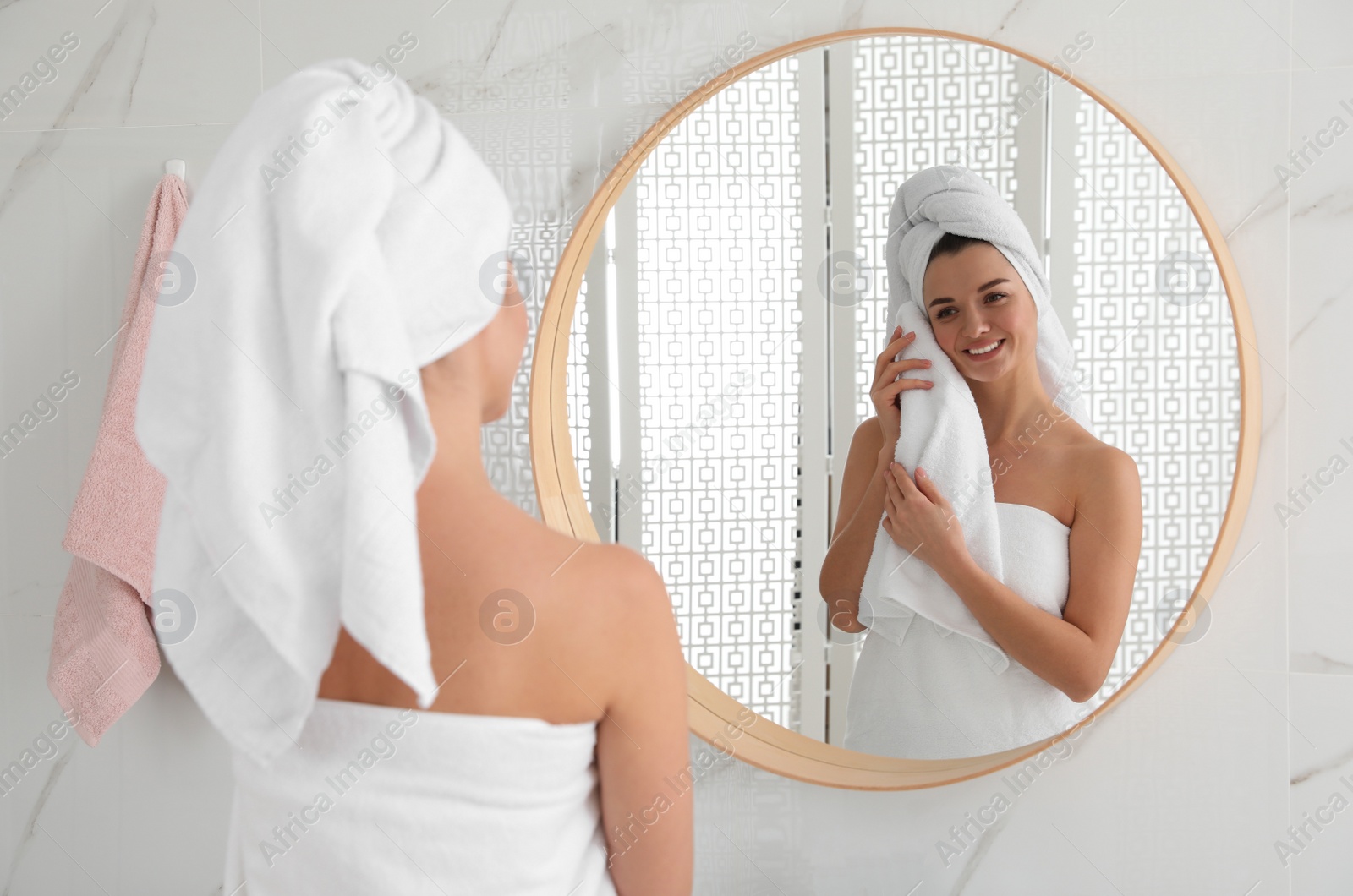 Photo of Beautiful young woman with hair wrapped in towel near mirror indoors