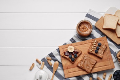 Different tasty toasts with nut butter and products on white wooden table, flat lay. Space for text