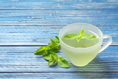 Photo of Cup with hot aromatic mint tea and fresh leaves on wooden table