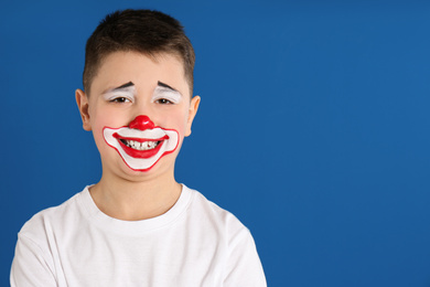 Preteen boy with clown makeup on blue background, space for text. April fool's day