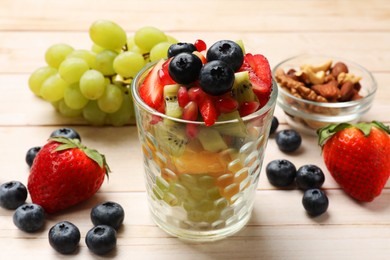 Photo of Healthy breakfast. Delicious fruit salad in glass and ingredients on light wooden table, closeup