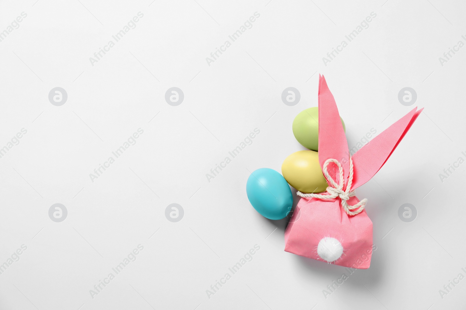 Photo of Easter bunny gift bag and dyed eggs on white background, top view