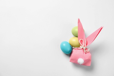 Photo of Easter bunny gift bag and dyed eggs on white background, top view