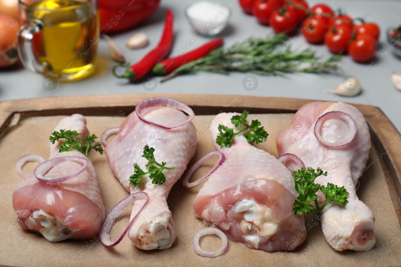 Photo of Raw chicken drumsticks with onion rings and parsley on wooden tray. Fresh meat