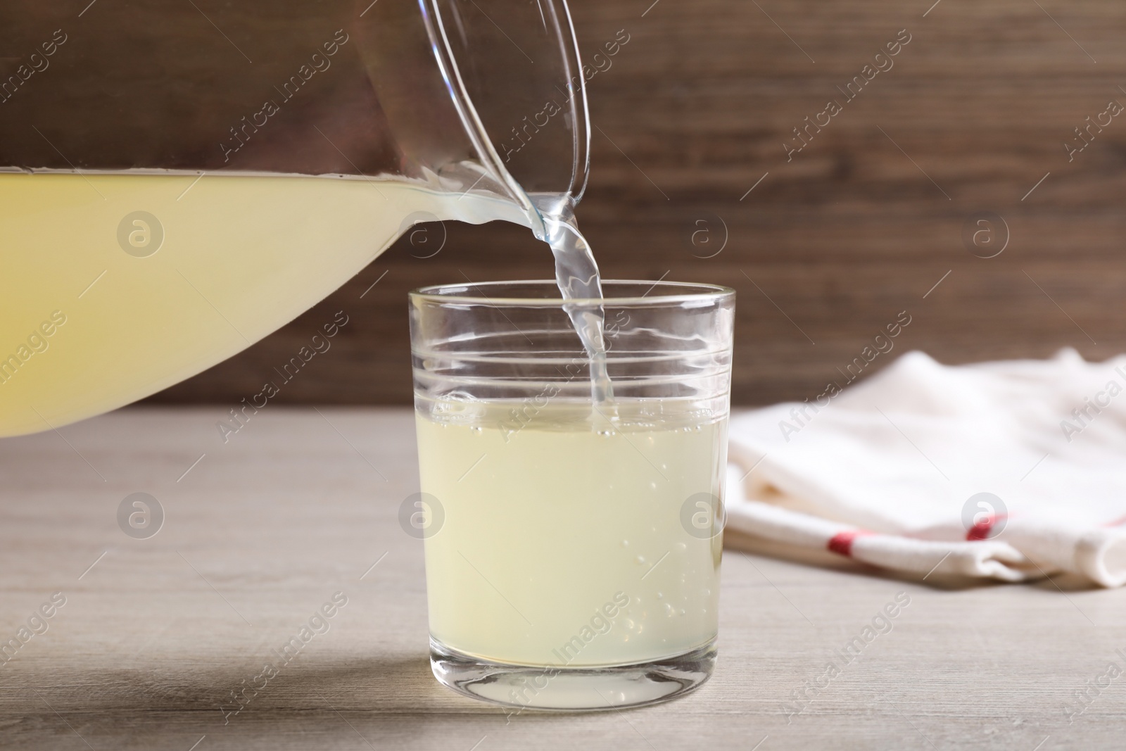 Photo of Pouring fresh juice from jug into glass on table