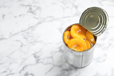 Photo of Tin can with conserved peach halves on marble background. Space for text