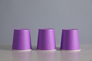 Photo of Shell game. Three purple cups on light table