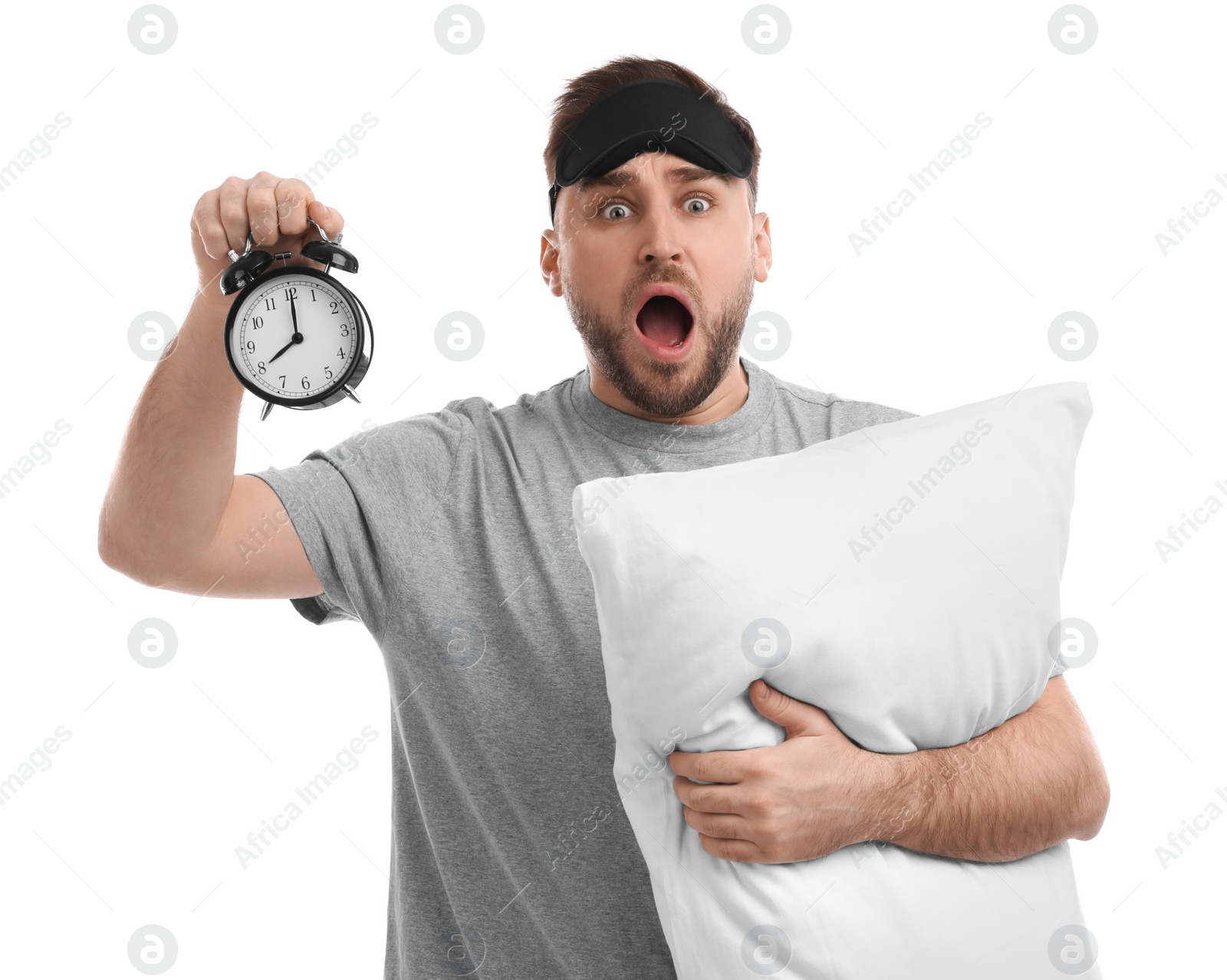 Photo of Emotional overslept man with alarm clock and pillow on white background. Being late concept