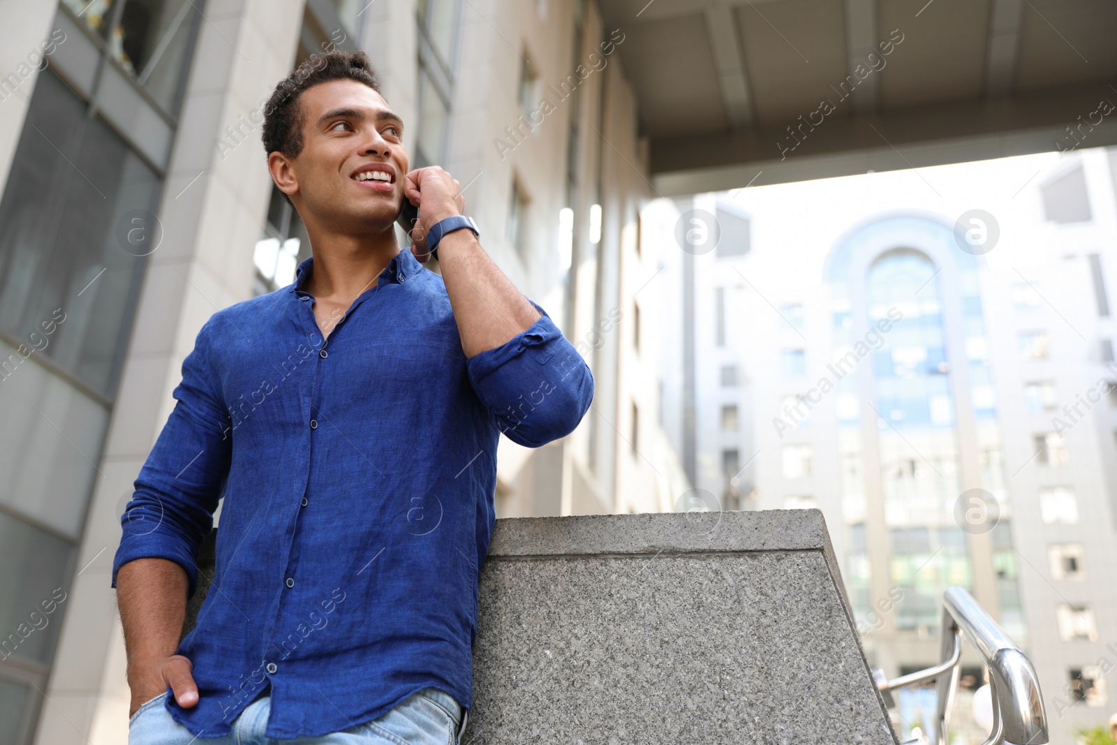 Photo of Handsome young African-American man talking on mobile phone outdoors, low angle view. Space for text