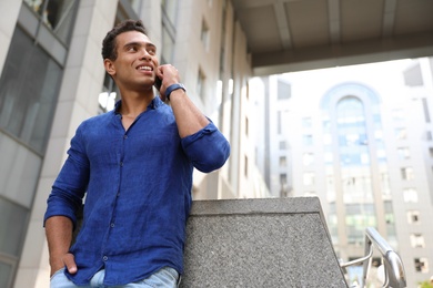 Photo of Handsome young African-American man talking on mobile phone outdoors, low angle view. Space for text