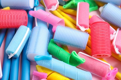 Many different hair curlers on pink background, closeup