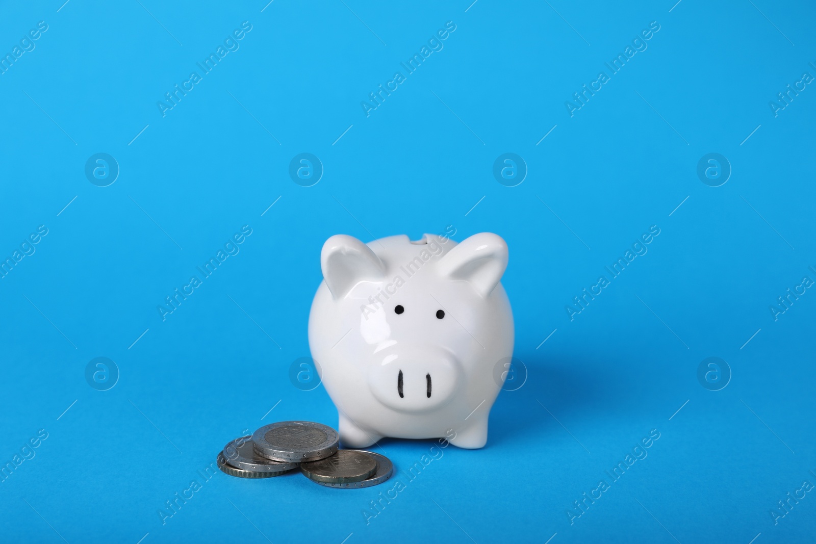 Photo of Ceramic piggy bank and coins on light blue background. Financial savings