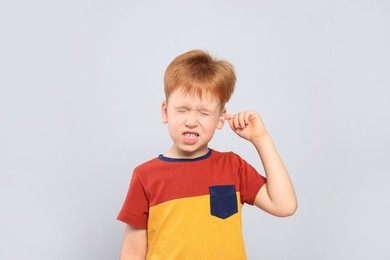 Little boy cleaning ear with cotton swab on light grey background