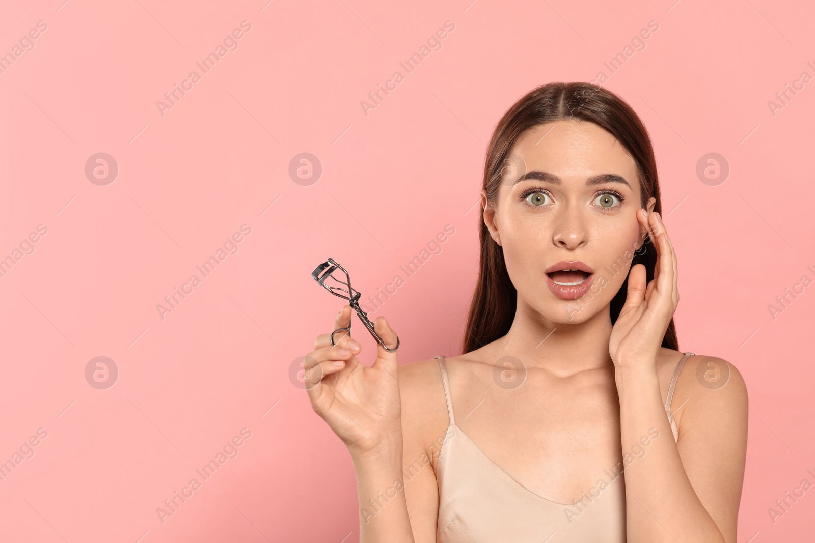 Photo of Emotional woman with eyelash curler on pink background, space for text