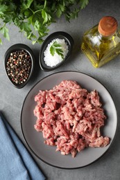 Photo of Raw ground meat, spices, parsley and oil on grey table, flat lay