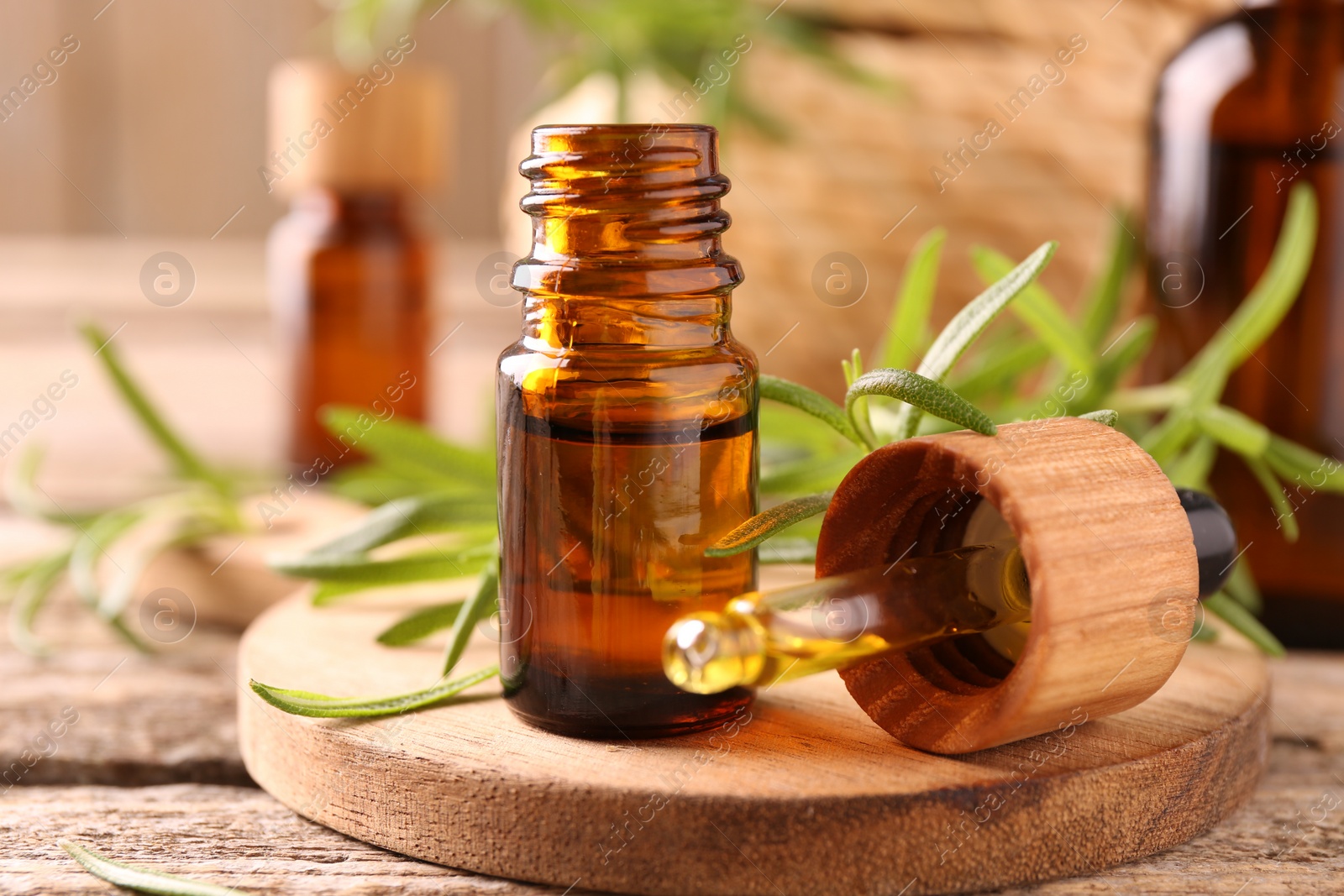 Photo of Aromatic essential oil in bottle, pipette and rosemary on wooden table, closeup