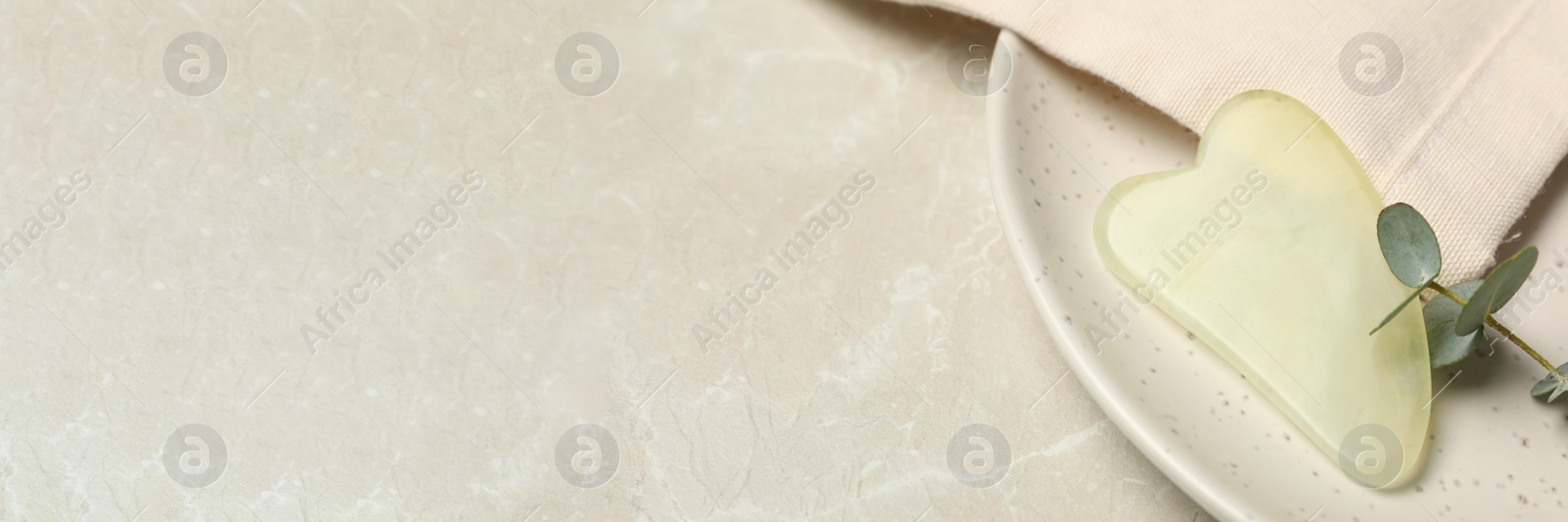 Image of Jade gua sha tool on light grey marble table, space for text. Banner design