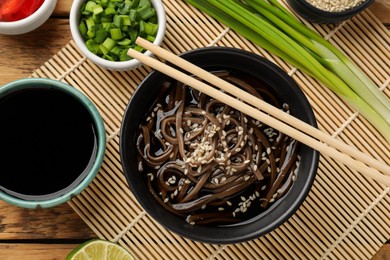 Photo of Tasty soup with buckwheat noodles (soba) and chopsticks served on wooden table, flat lay