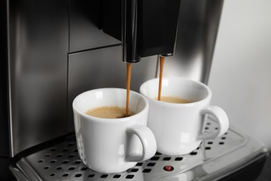 Photo of Espresso machine pouring coffee into cups against light background, closeup