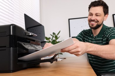 Photo of Man using modern printer at wooden table indoors, selective focus