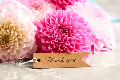 Photo of Paper tag with phrase Thank You and bouquet of dahlias on marble table, closeup