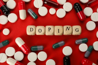 Wooden cubes with word Doping and drugs on red background, flat lay