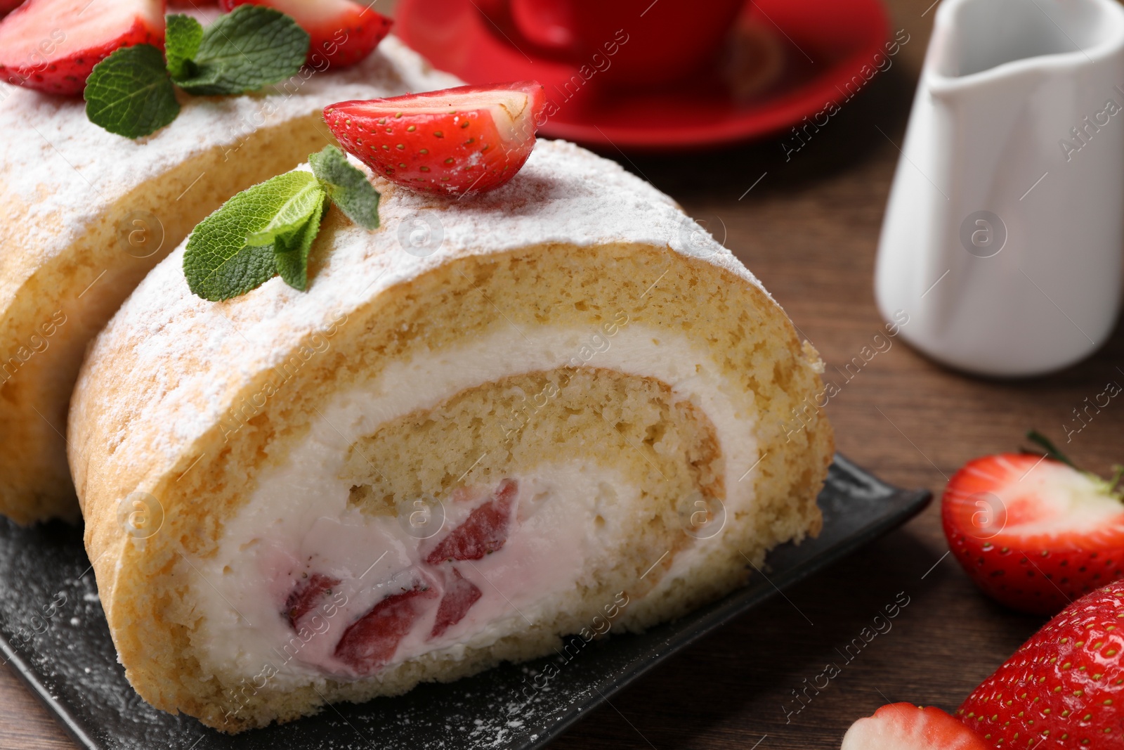 Photo of Delicious cake roll with strawberries and cream on black board, closeup