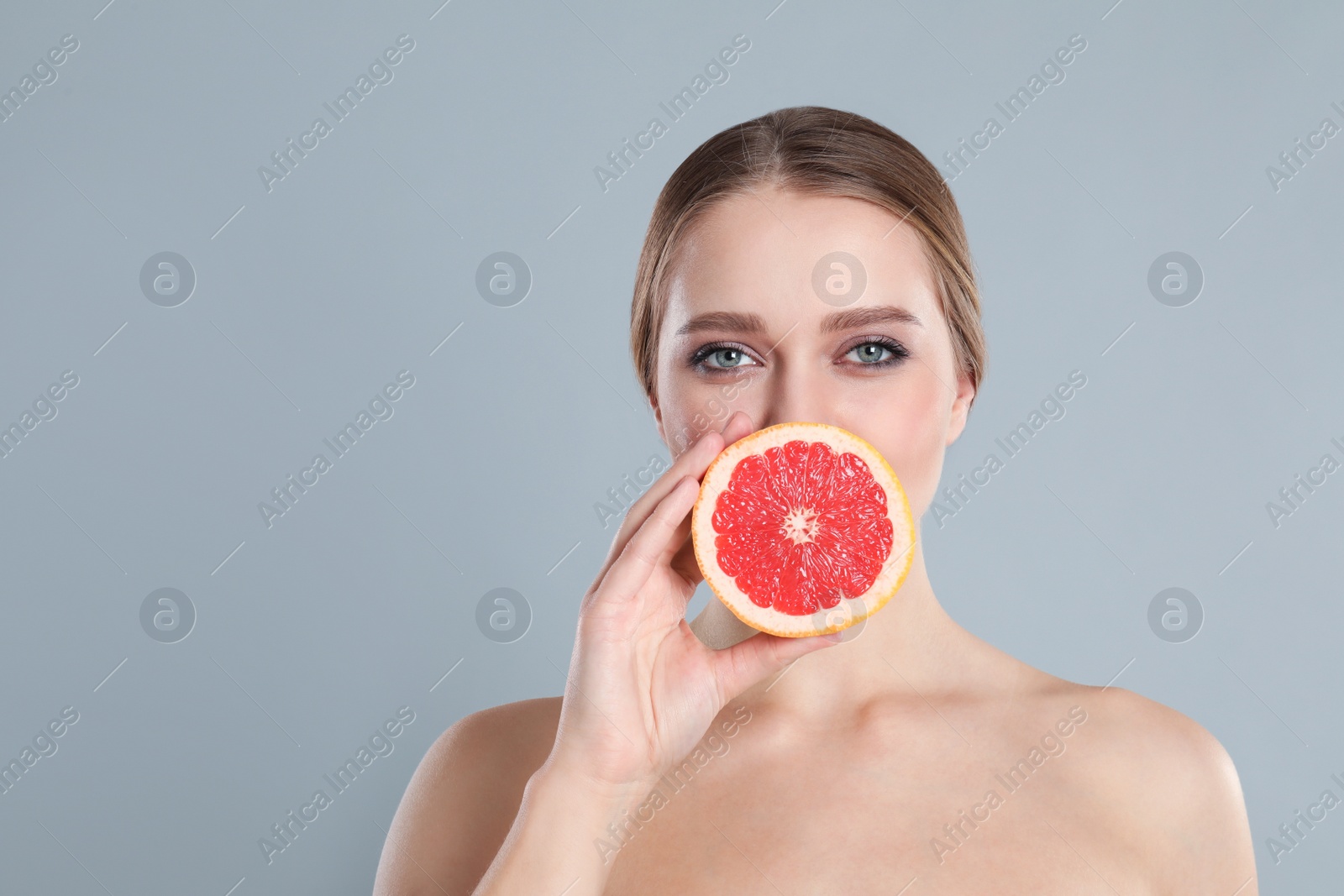 Photo of Young woman with cut grapefruit on grey background. Vitamin rich food