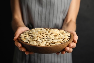 Photo of Young woman with bowl of raw pumpkin seeds on black background, closeup