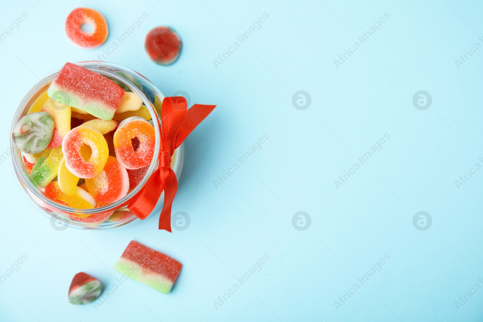 Photo of Glass jar with tasty colorful jelly candies on light blue background, top view. Space for text