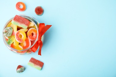 Photo of Glass jar with tasty colorful jelly candies on light blue background, top view. Space for text