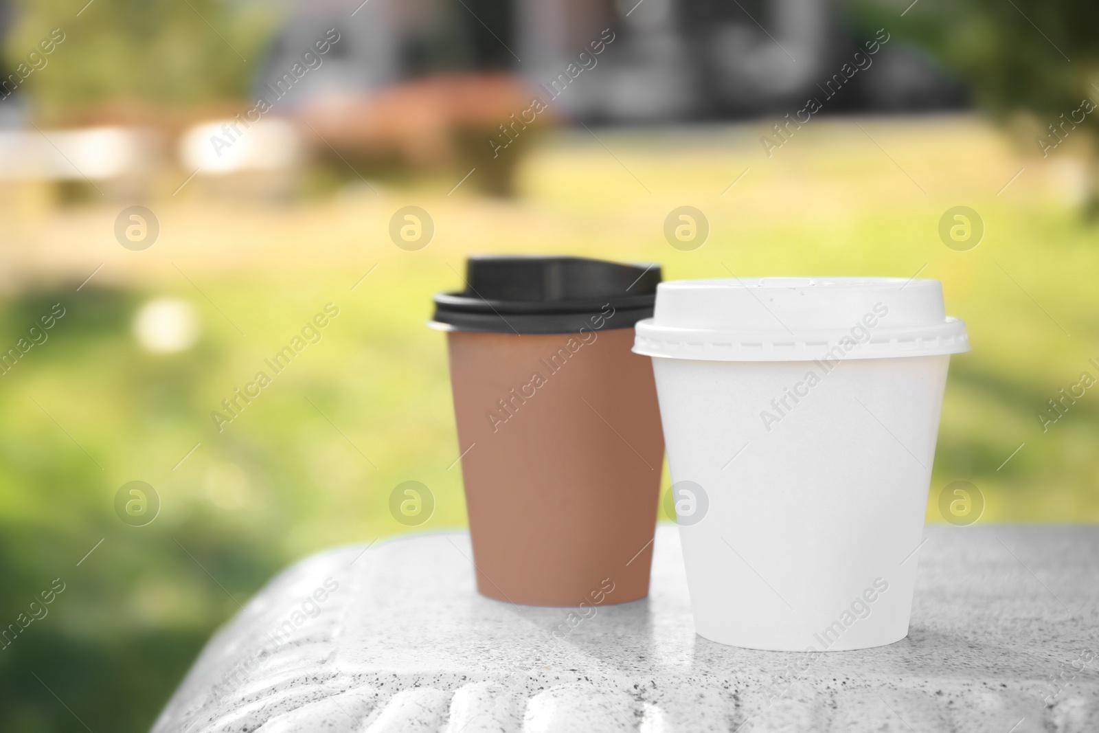 Photo of Cardboard cups with tasty coffee on stone bench outdoors, closeup