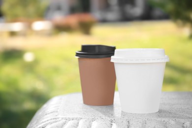 Cardboard cups with tasty coffee on stone bench outdoors, closeup