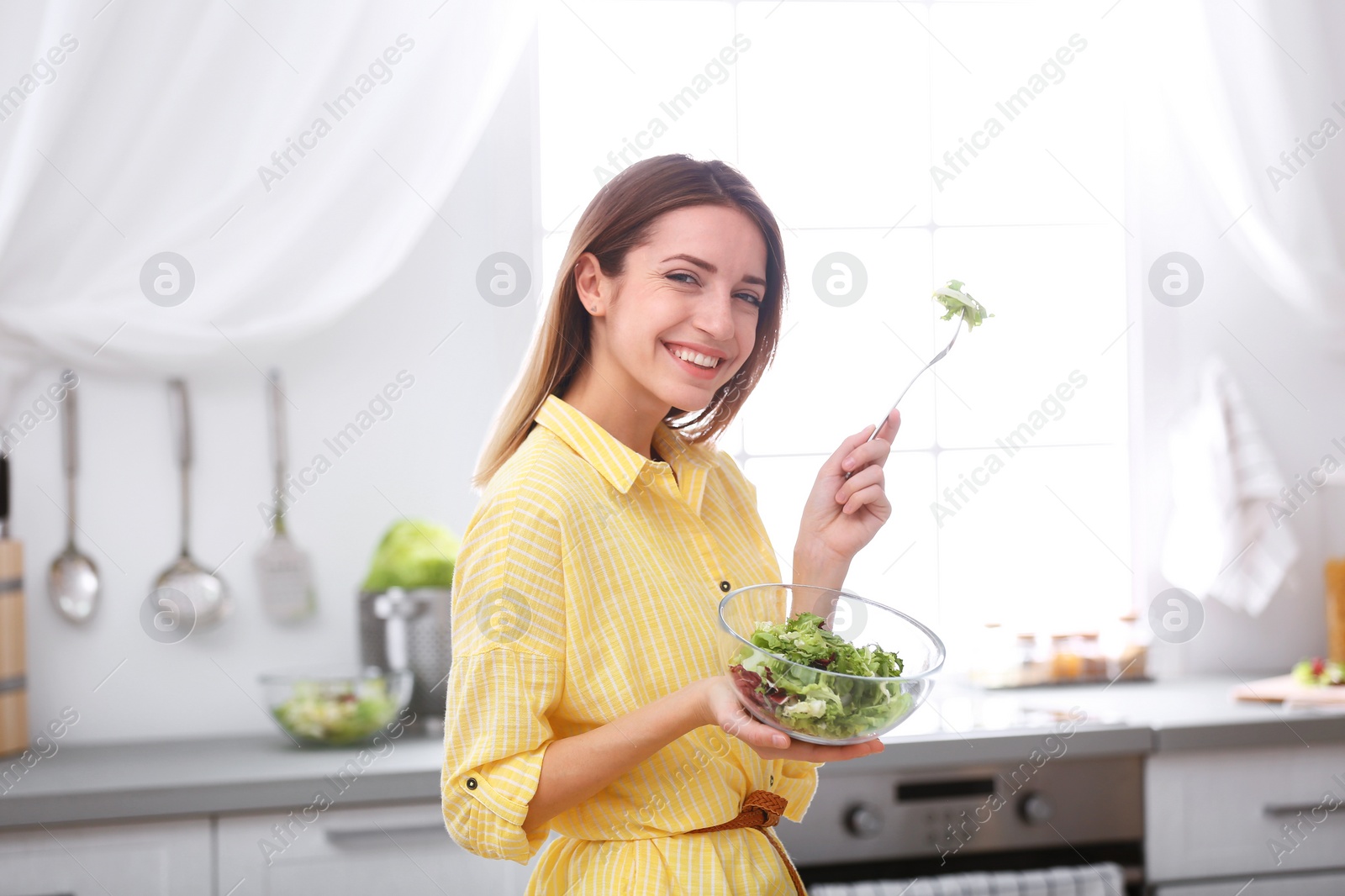 Photo of Happy young woman eating salad in kitchen. Healthy diet