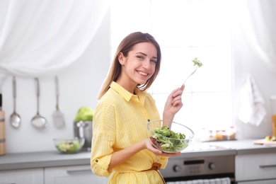 Happy young woman eating salad in kitchen. Healthy diet