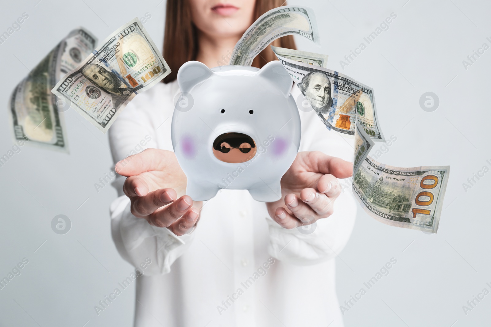 Image of Young woman holding piggy bank and American dollars falling on light background, closeup 