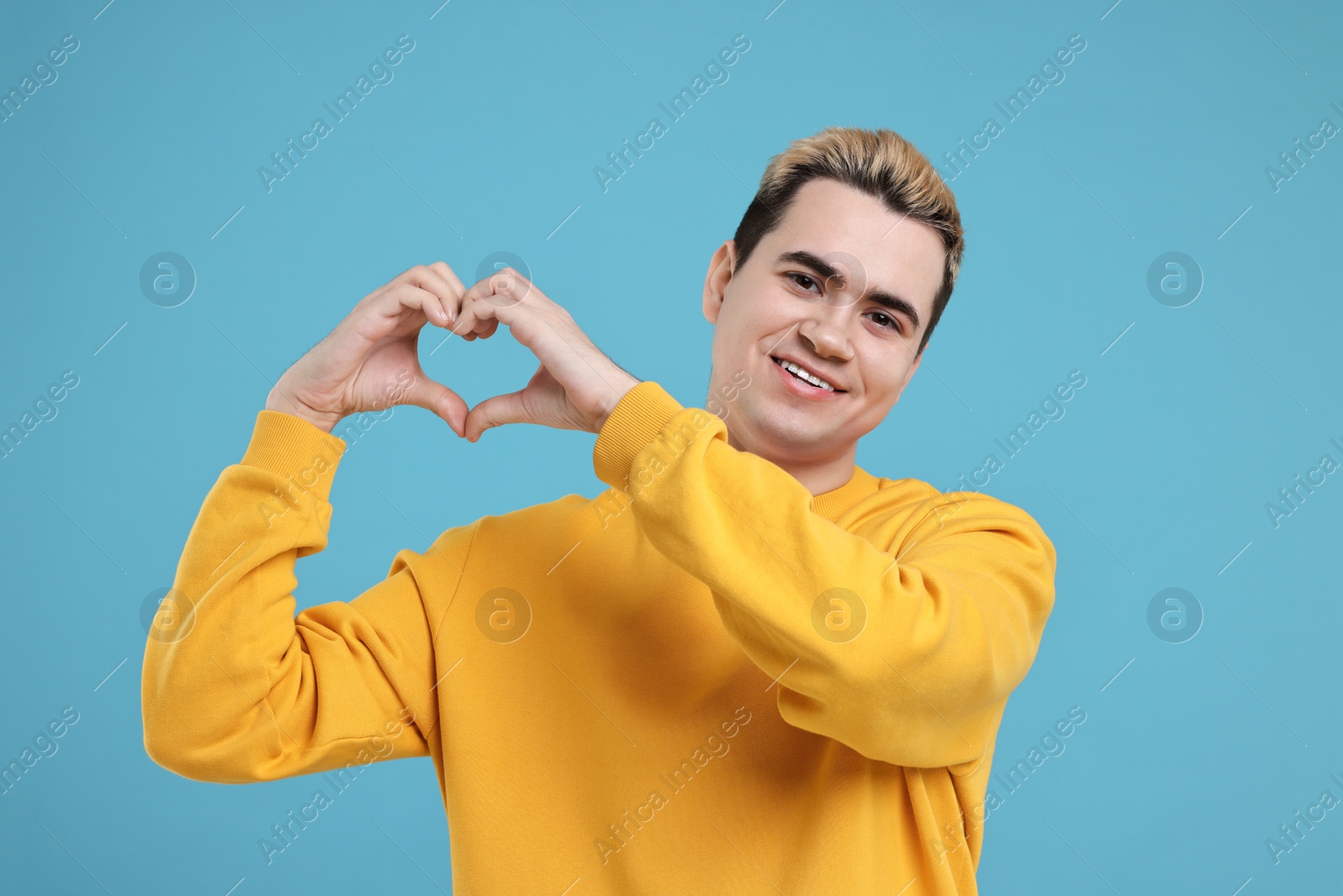 Photo of Young man showing heart gesture with hands on light blue background