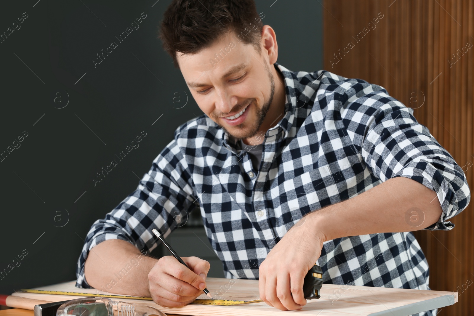 Photo of Handsome working man making marks on timber at table indoors. Home repair