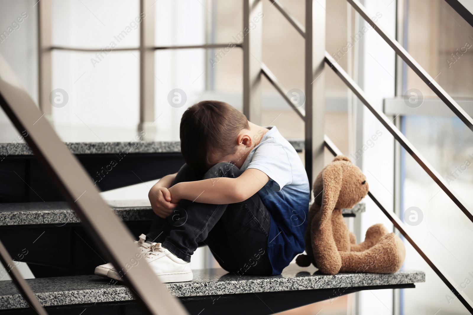 Photo of Sad little boy with toy sitting on stairs indoors