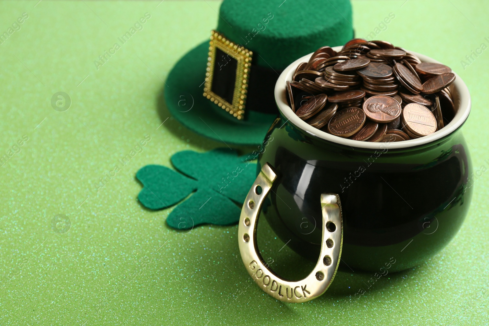 Photo of Pot of gold coins, horseshoe, hat and clover on green background, space for text. St. Patrick's Day celebration