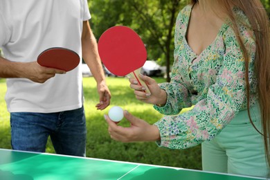 Photo of Couple with tennis rackets and ball near ping pong table in park, closeup