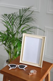 Photo of Empty photo frame, sunglasses and watch on wooden table indoors