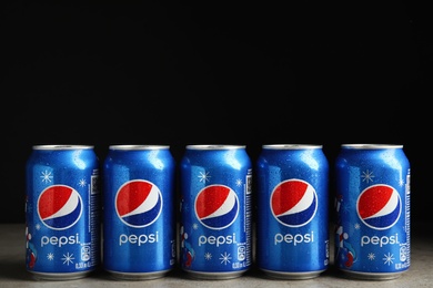 MYKOLAIV, UKRAINE - FEBRUARY 9, 2021: Many cans of Pepsi on table against black background, space for text