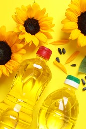 Bottles of cooking oil, sunflowers and seeds on yellow background, flat lay