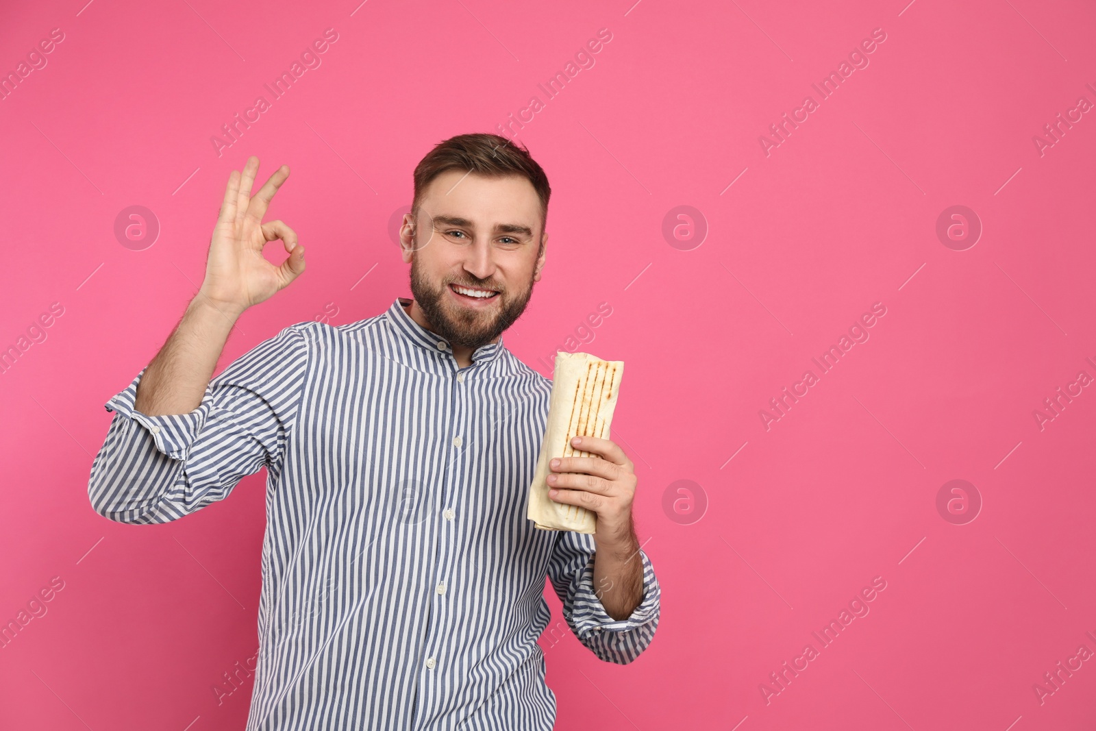 Photo of Young man with delicious shawarma on pink background, space for text