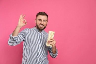 Young man with delicious shawarma on pink background, space for text