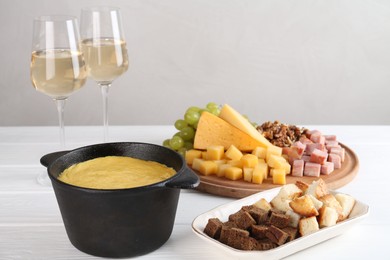 Photo of Fondue with tasty melted cheese, different products and aromatic wine in glasses on white wooden table