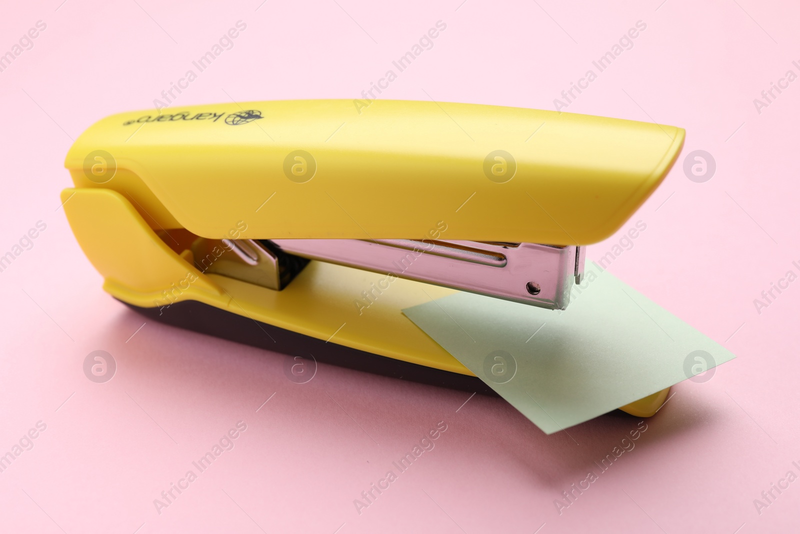 Photo of One yellow stapler on pink background, closeup
