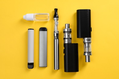 Different electronic cigarettes and vaping liquid on yellow background, flat lay