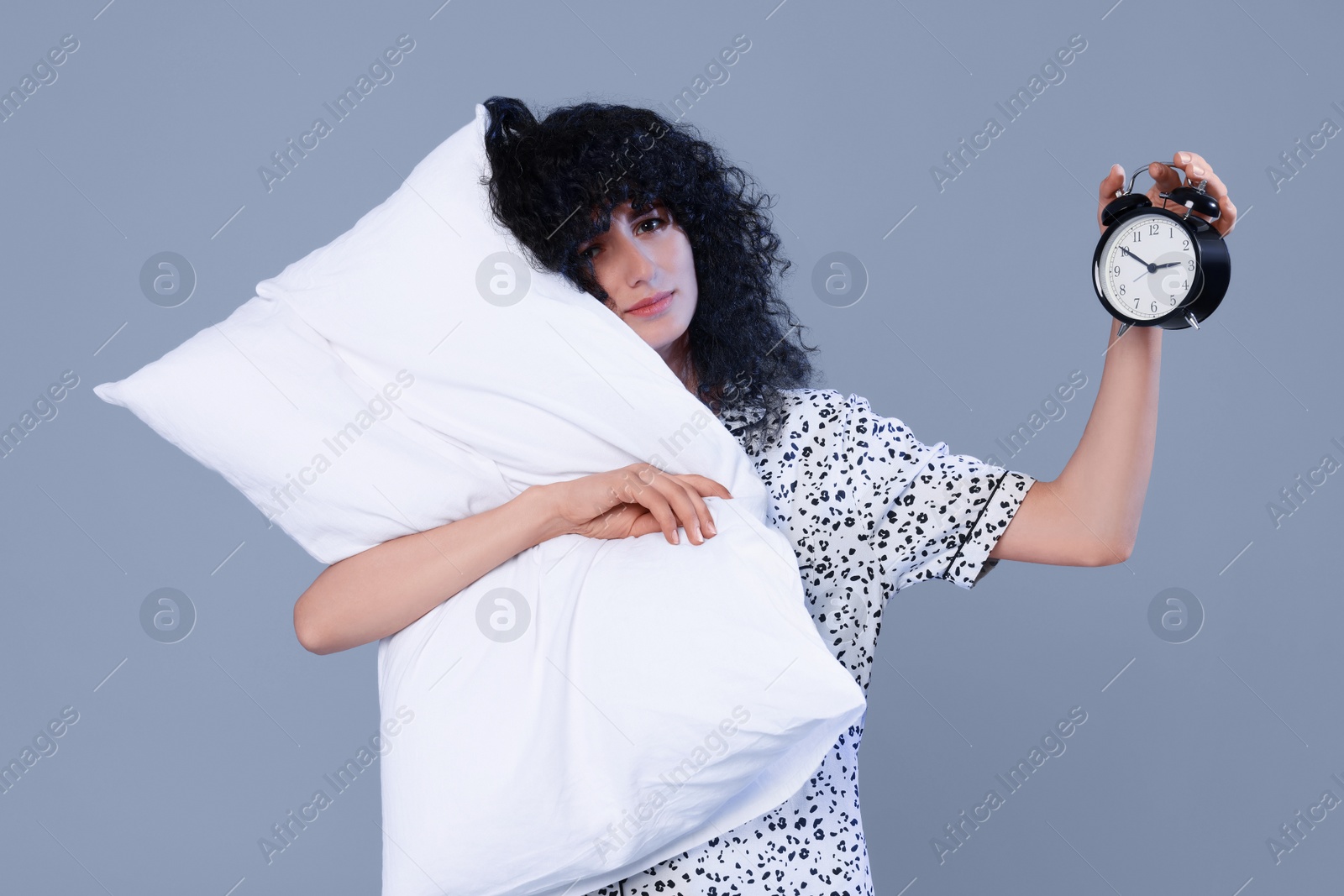 Photo of Tired young woman with pillow and alarm clock on light grey background. Insomnia problem